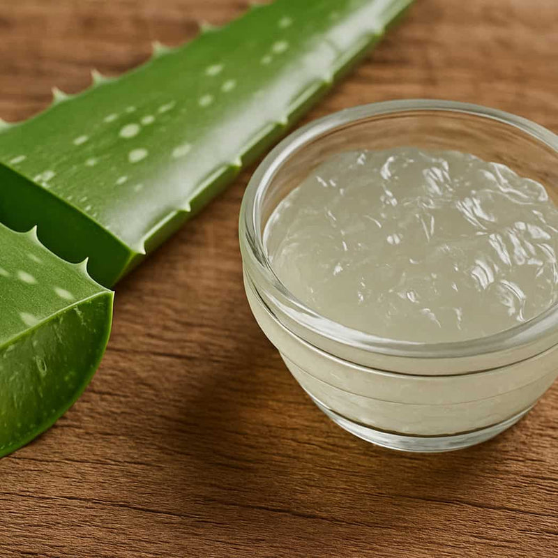 Glass bowl of aloe vera gel with fresh aloe leaves on a wooden surface