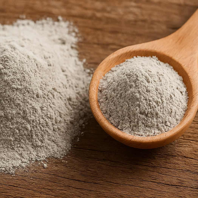 Wooden spoon filled with gray bentonite clay powder on a wooden surface