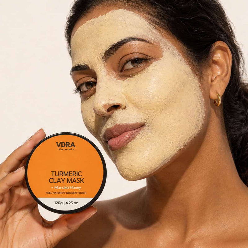 Woman with melanin-rich skin applying VDRA turmeric clay mask for dark spots