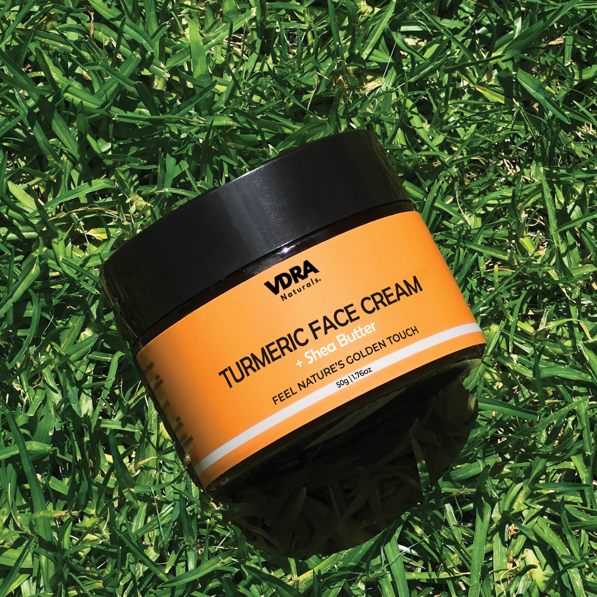 A jar of turmeric face cream moisturizer with shea butter, placed on a grassy surface, under natural light.