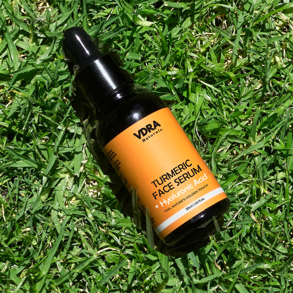A bottle of Skin Brightening Turmeric Face Serum with Vitamin C and Hyaluronic Acid, placed on a grassy surface.