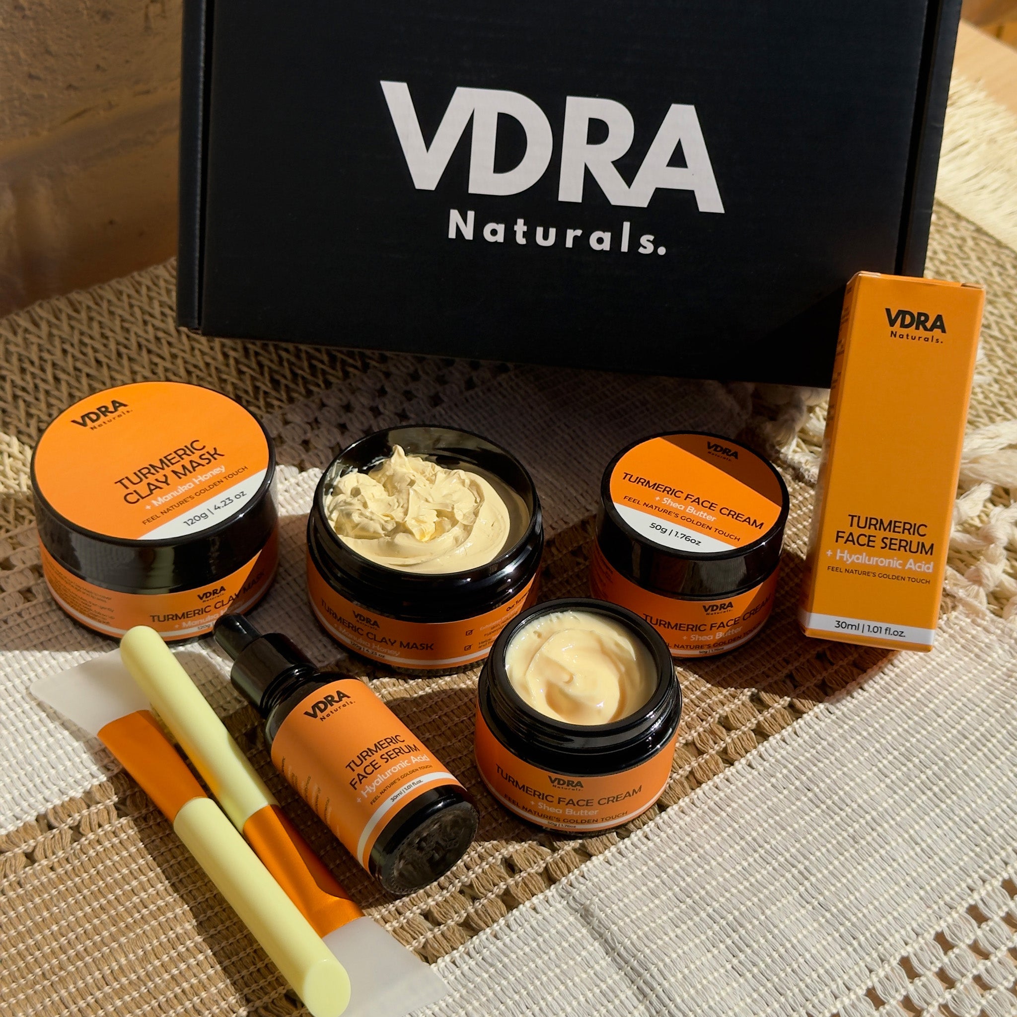 VDRA Naturals skincare products including jars and a serum on a textured surface.