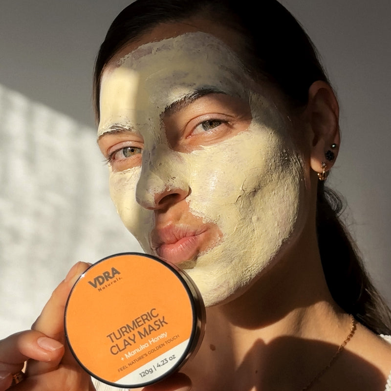 Woman with VDRA's  turmeric clay mask applied on her face holding a VDRA clay mask.