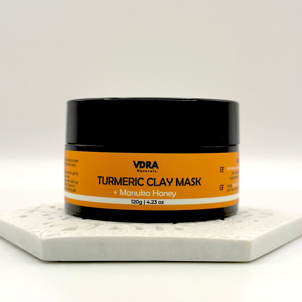 Jar of VDRA Naturals Turmeric Clay Mask with Manuka Honey on a white surface and a white background.