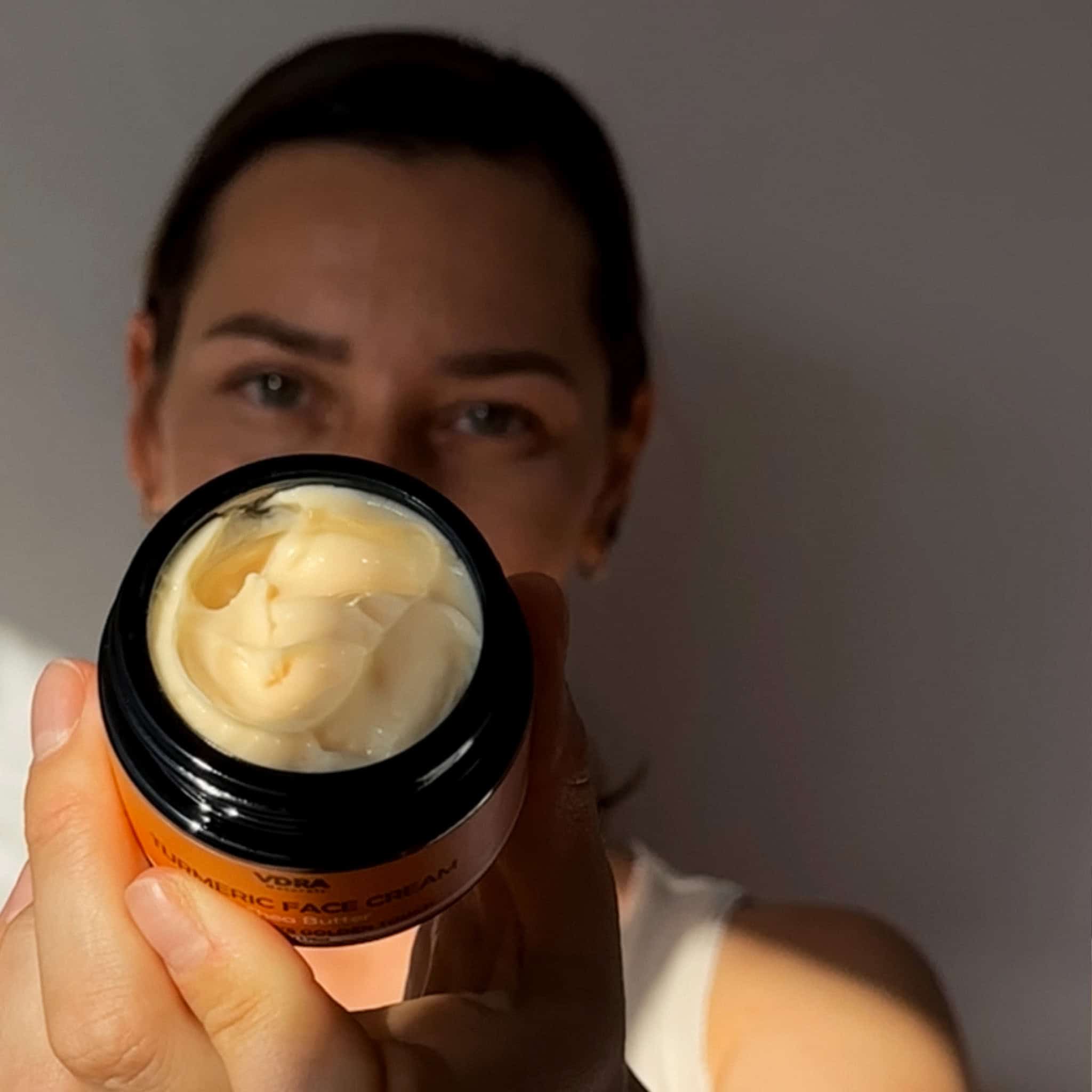 A model holding up the jar of the  turmeric face cream to the camera.