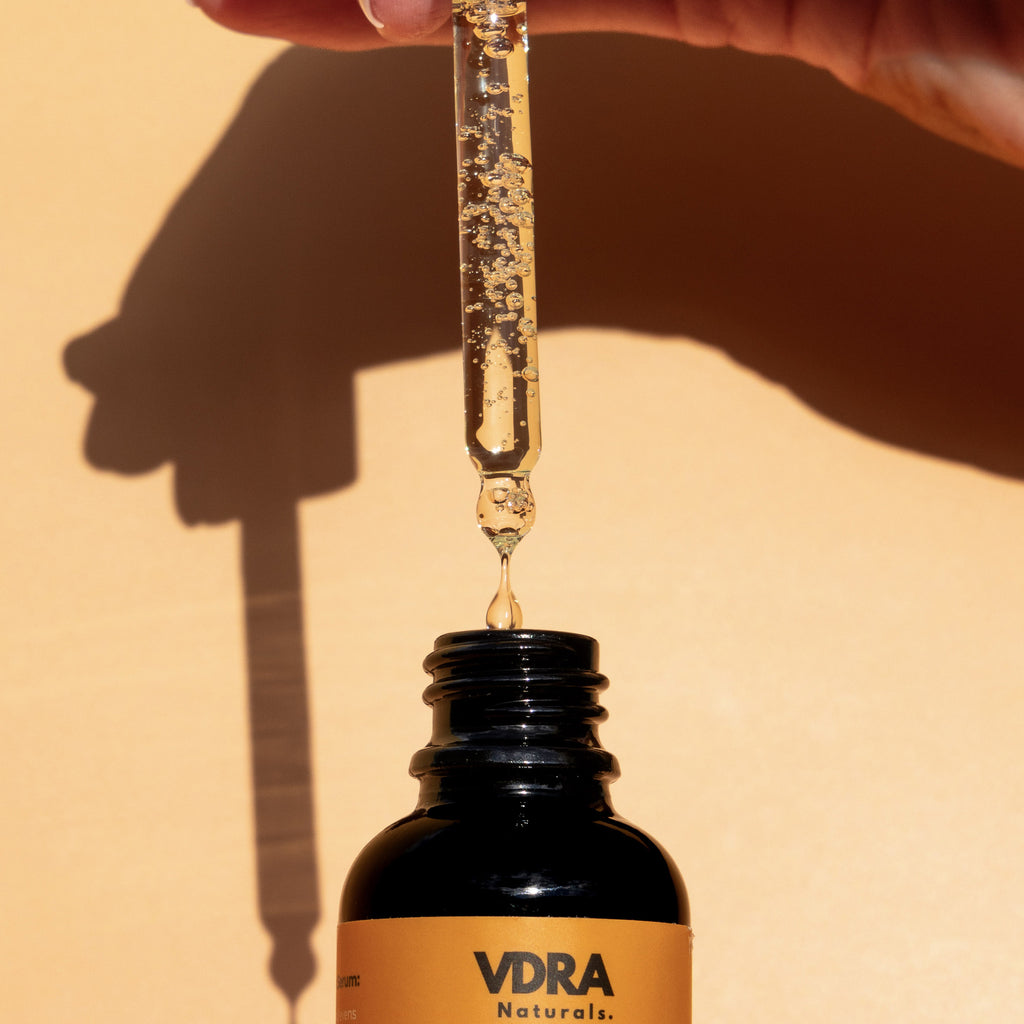 VDRA Naturals turmeric face serum with a droplet being dispensed into the bottle against a beige background